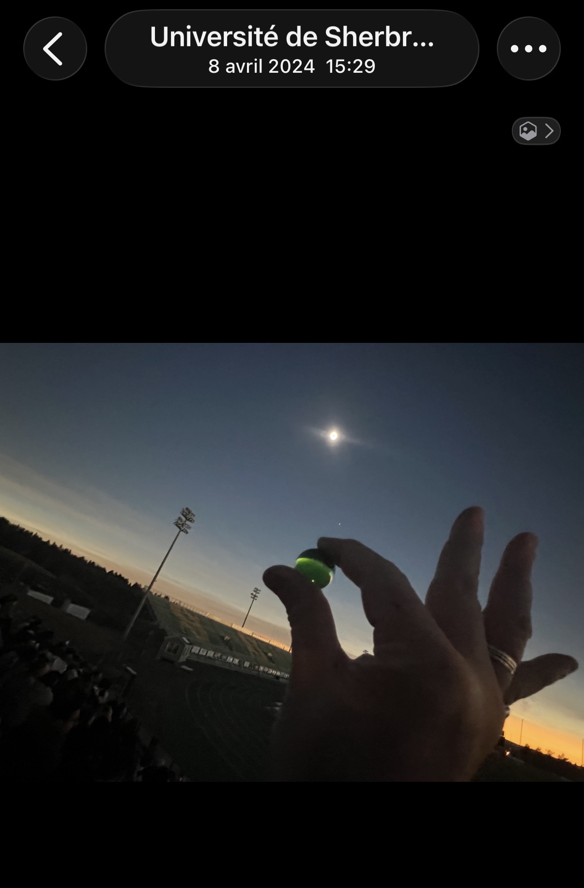 La Perle Verte lumineuse tenue vers le ciel, le soleil éclipsé formant un anneau au-dessus, le stade baignant dans une lumière dorée d'horizon.